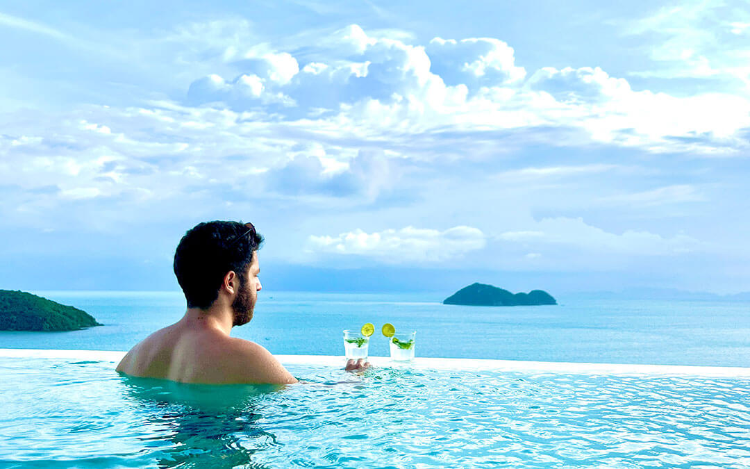 Man in pool drinking cocktails and looking at the ocean