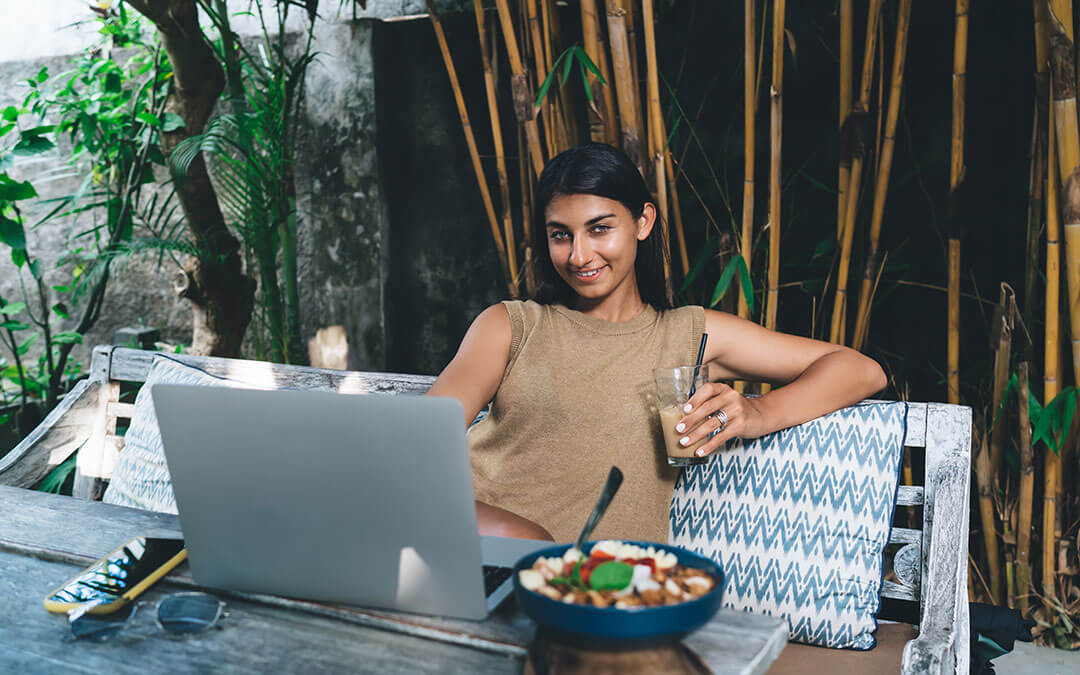 Digital nomad sitting at cafe eating salad and working on laptop