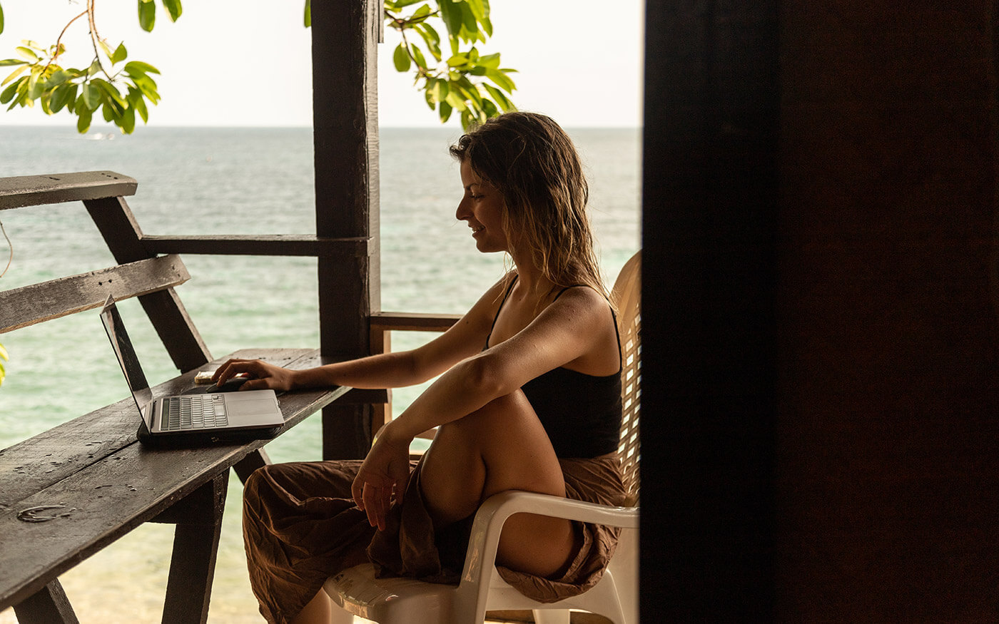 Digital nomad woman at the beach tying on laptop