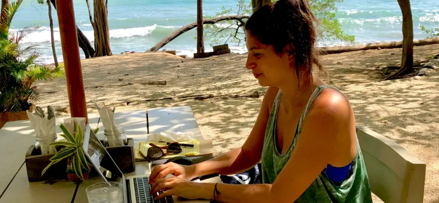 A woman working on a laptop at a beachside table overlooking the ocean in Las Catalinas, Costa Rica