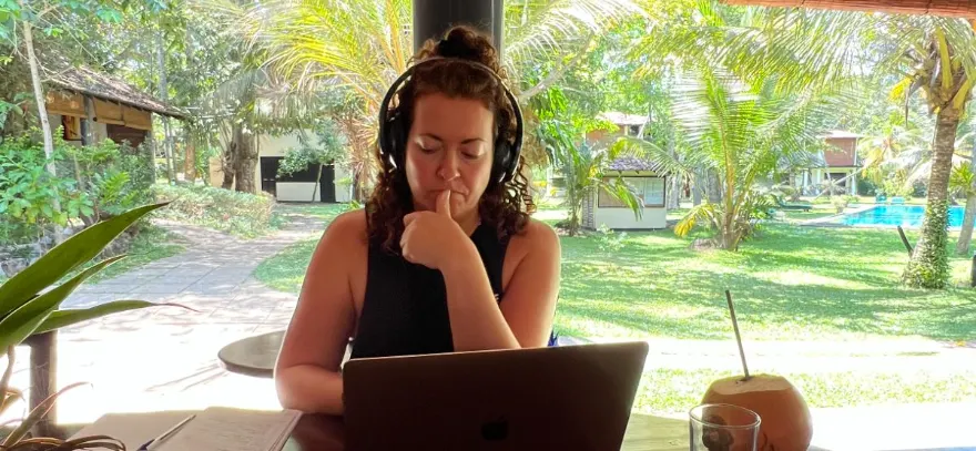 A woman in headphones working on a laptop under an open-air pavilion in Sri Lanka