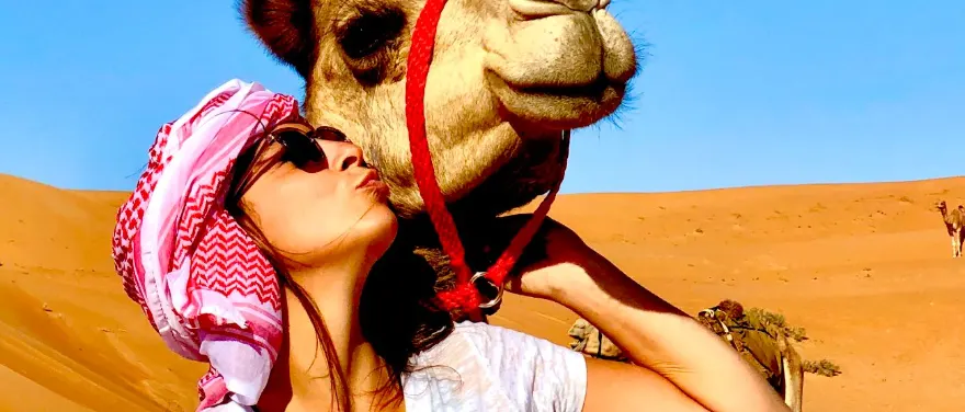 Traveler in a headscarf kissing a camel in the desert near Cairo, Egypt