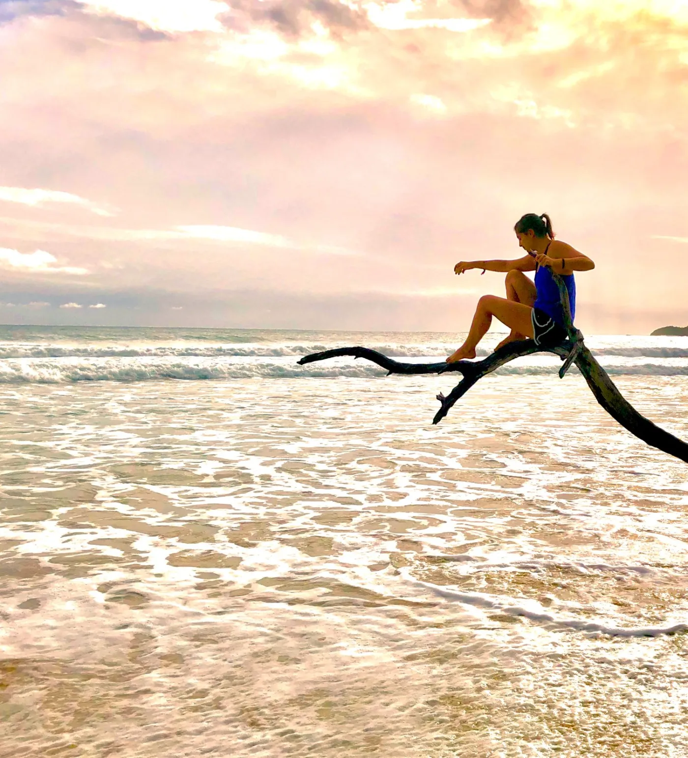 A traveler sitting on driftwood over the surf at sunset in Bocas del Toro, Panama
