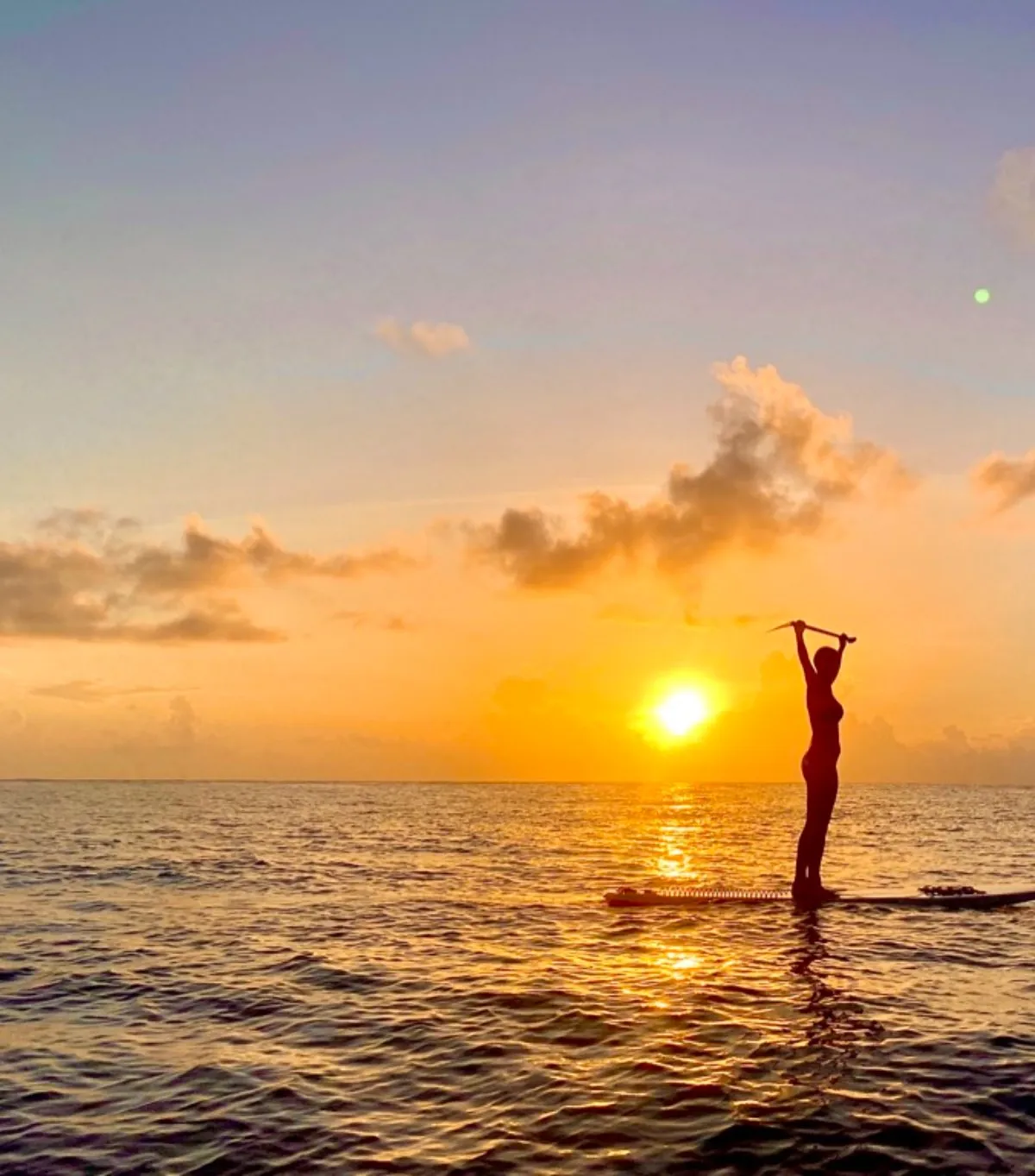 A paddleboarder silhouetted against a golden sunset over the ocean in Bali, Indonesia