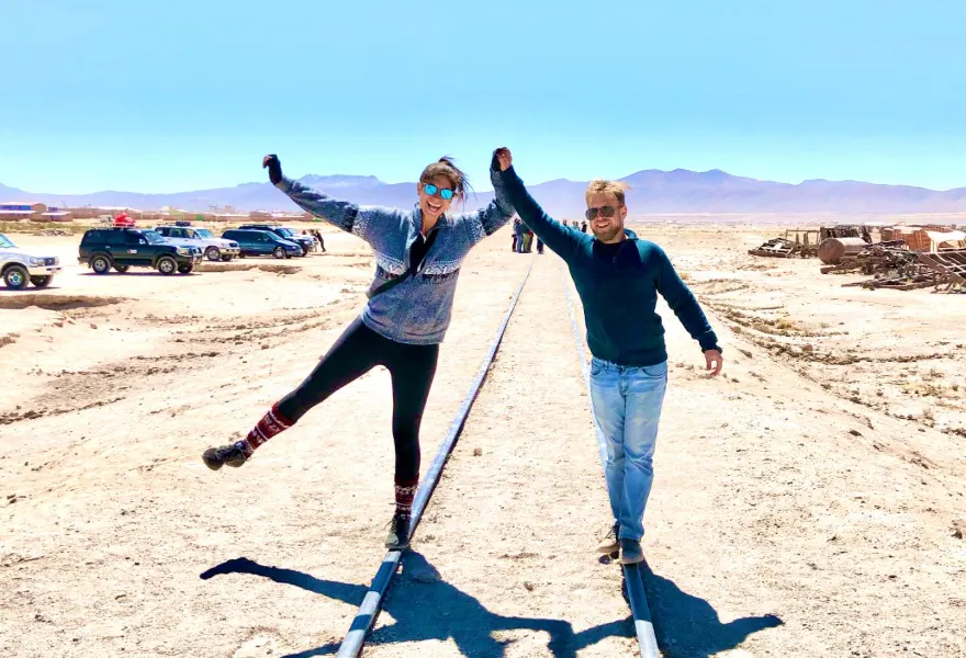 Two travelers balancing on railway tracks under a wide blue sky in La Paz, Bolivia