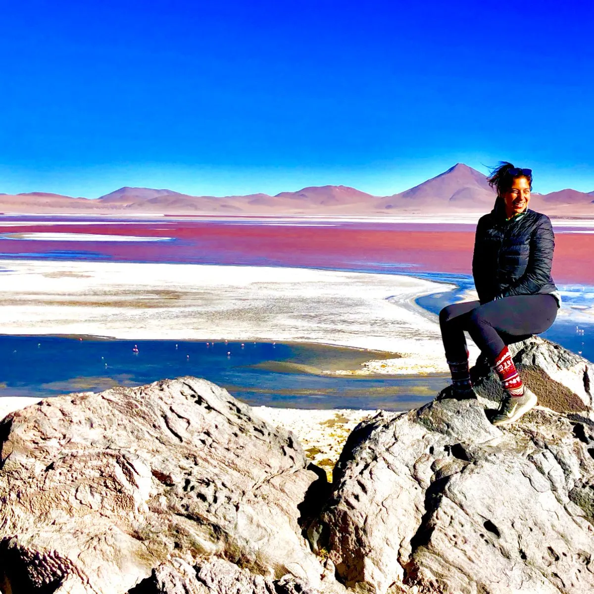 A traveler sitting on a rock above the red lagoon and flamingos at Salar de Uyuni, Bolivia